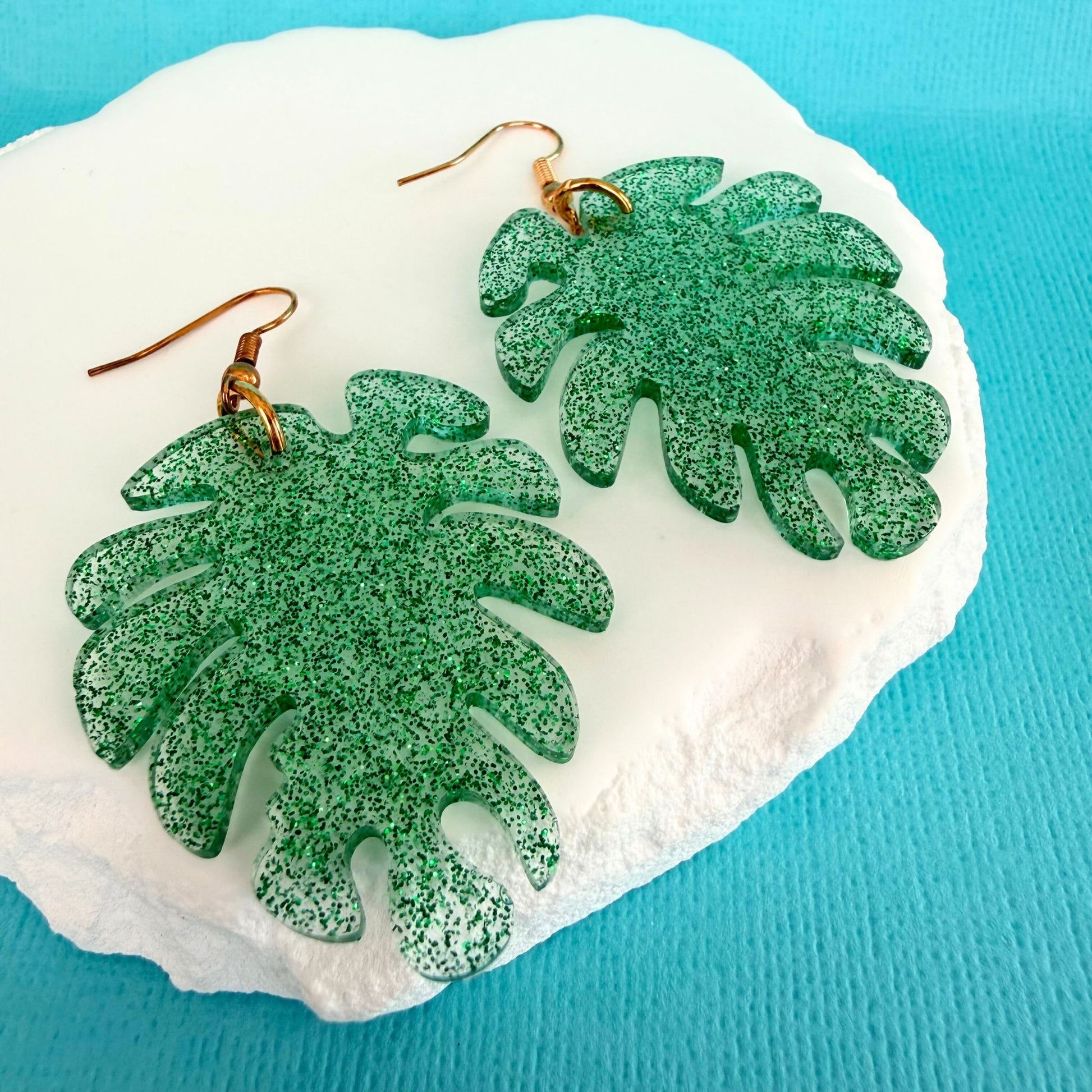 Green leaf-shaped handmade resin earrings on a white stone with a blue background.