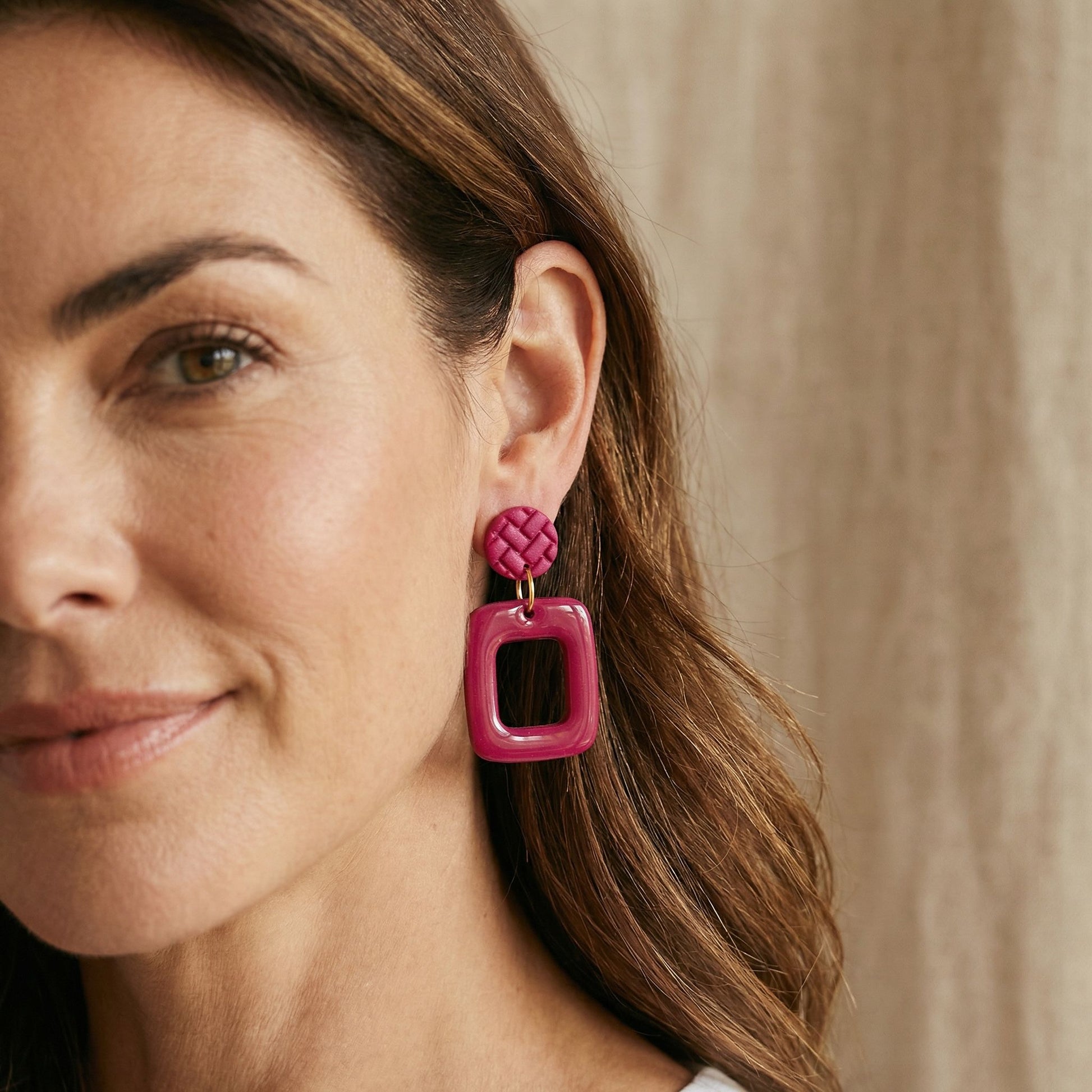 Close-up of a woman wearing magenta handmade Australian frame shaped drop earrings with a neutral background.