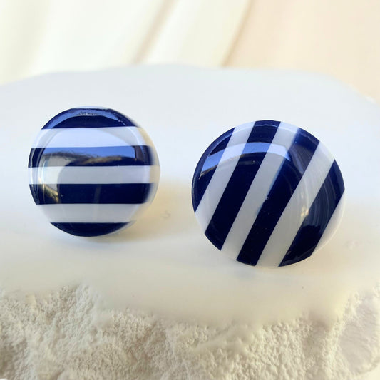Pair of navy blue and white striped stud earrings on a textured surface.