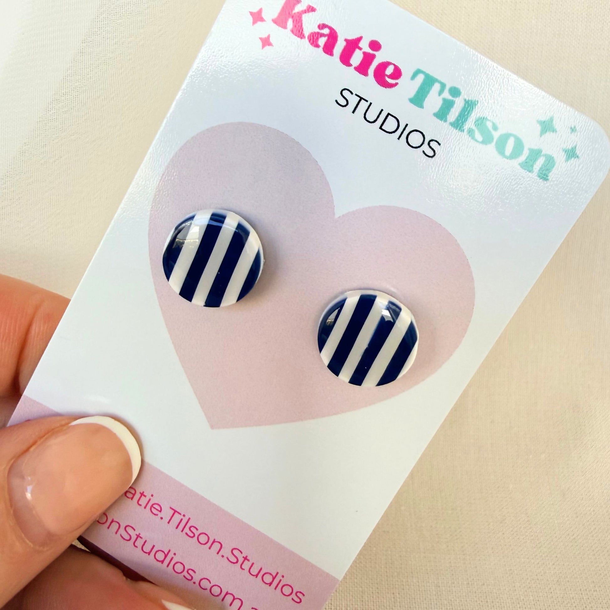 Katie Tilson Studios stud earrings with navy and white striped design on an earring card held by a hand.