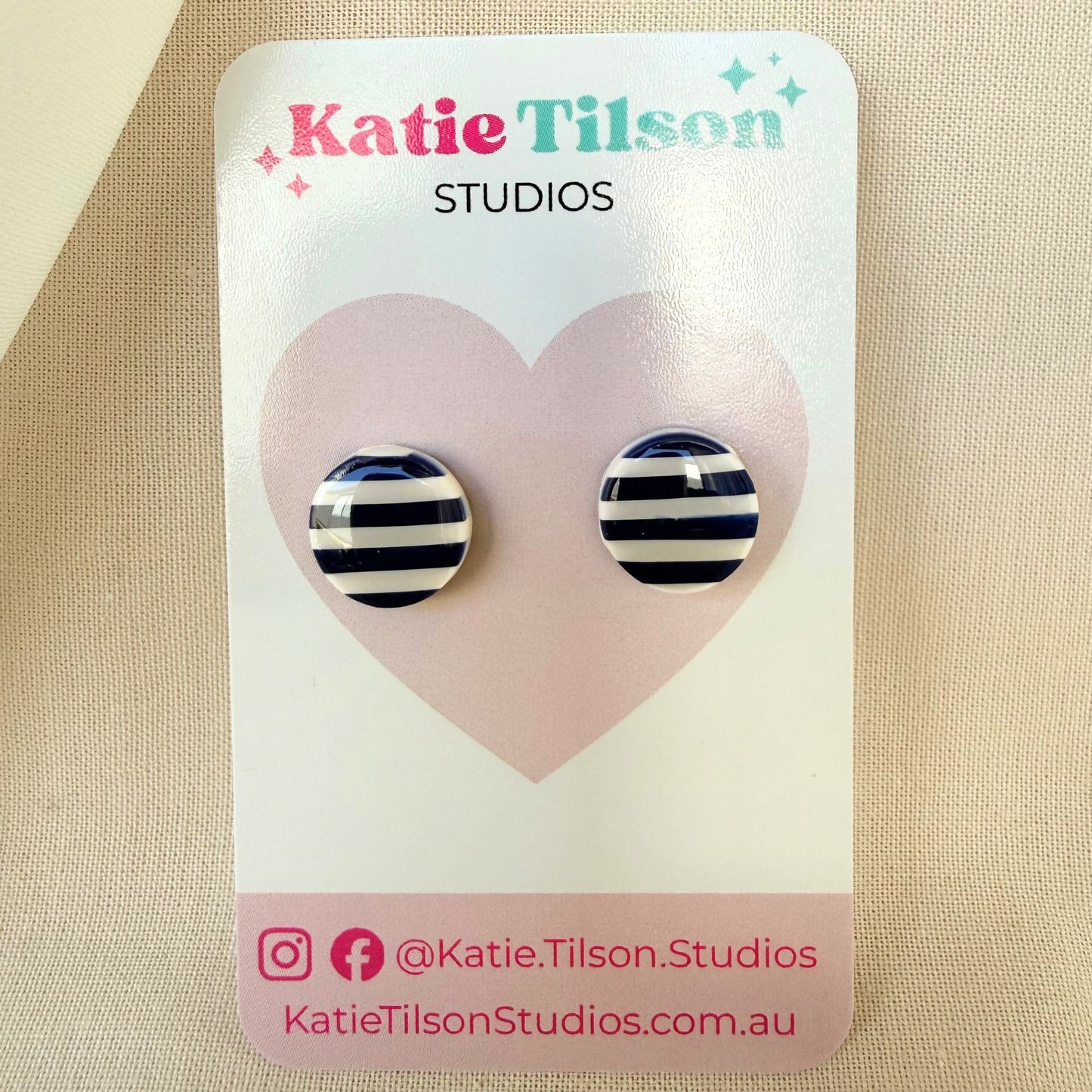 Navy blue and white striped circular stud earrings on a Katie Tilson Studios card against a beige background.