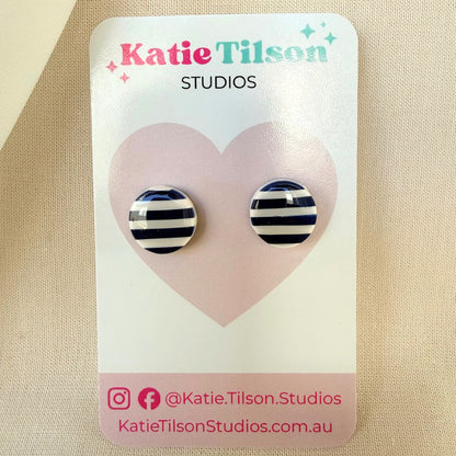 Navy blue and white striped circular stud earrings on a Katie Tilson Studios card against a beige background.