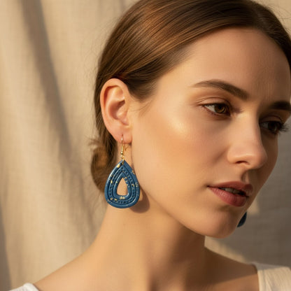 Woman wearing Australian handmade blue teardrop dangle earrings with gold flecks in front of a neutral background.