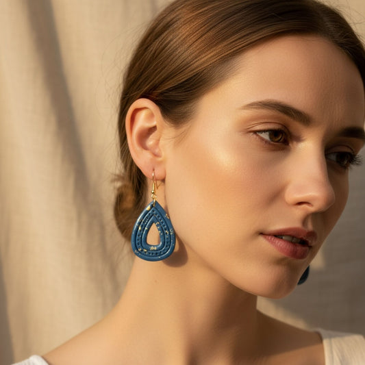 Woman wearing Australian handmade blue teardrop dangle earrings with gold flecks in front of a neutral background.