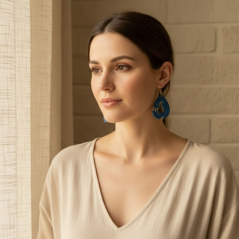 Woman wearing Australian handmade blue dangle earrings with gold flecks in a softly lit room.