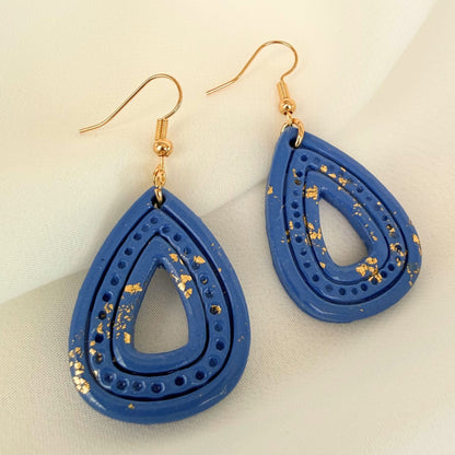 Australian handmade dangle earrings Ocean Gleam Teardrops in blue with gold leaf flat lay on white fabric. 