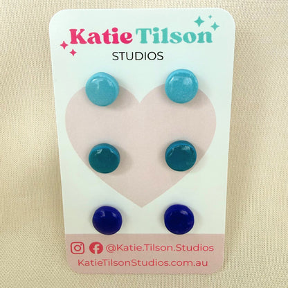 Aqua, teal and cobalt blue circular stud earrings displayed on a Katie Tilson Studios branded card against a beige background.