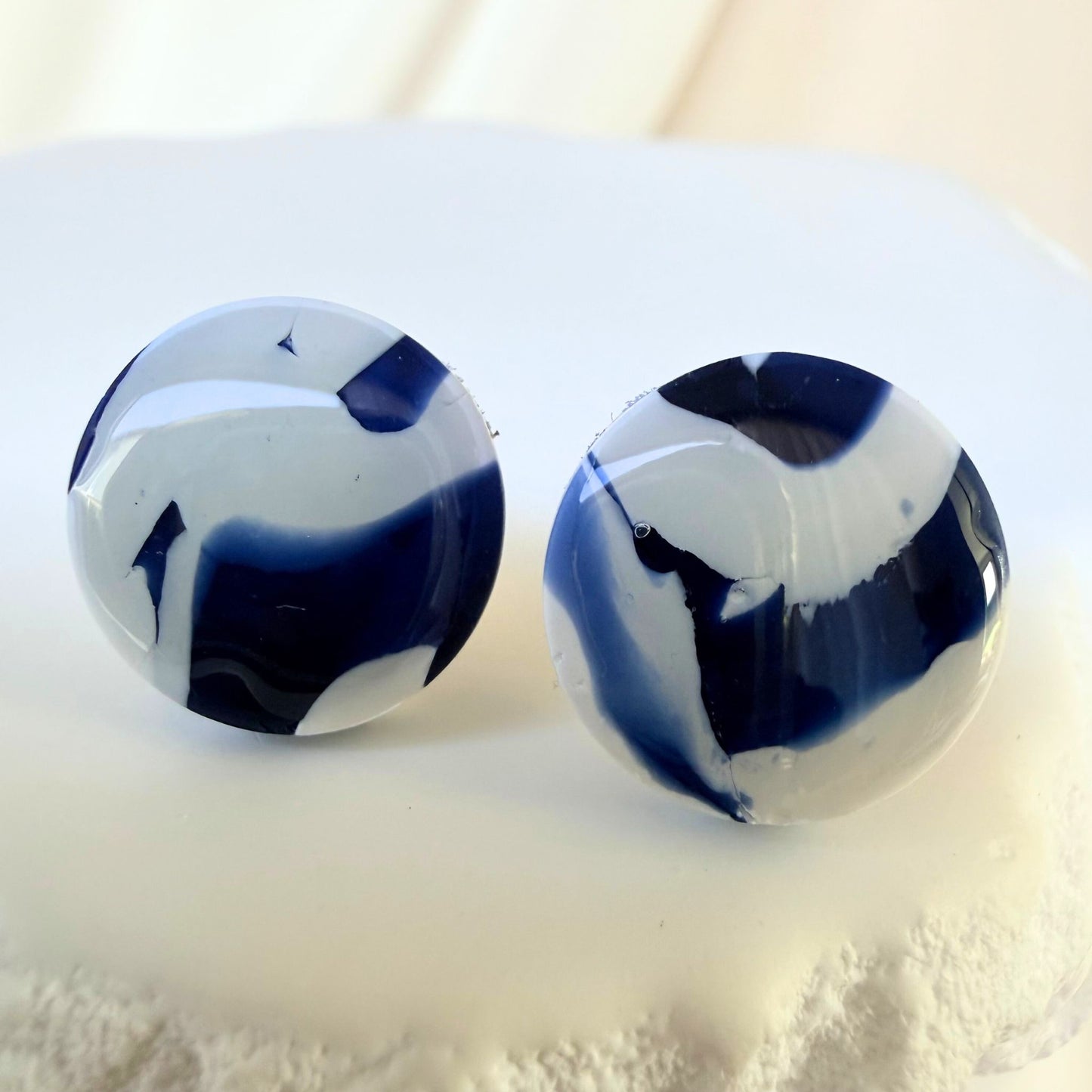 Pair of blue and white circular stud marbled earrings on a light background.