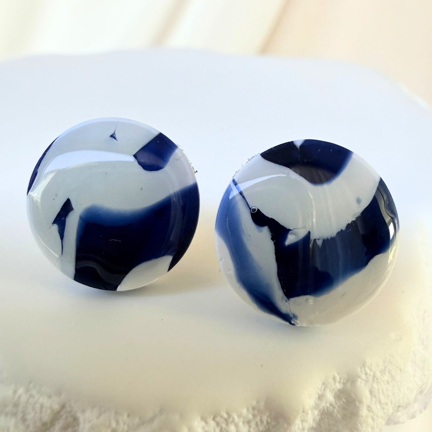 Pair of blue and white circular stud marbled earrings on a light background.
