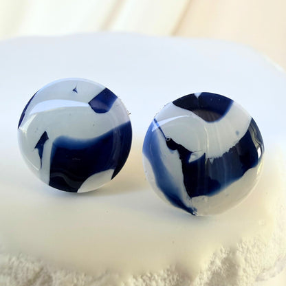 Pair of blue and white circular stud marbled earrings on a light background.
