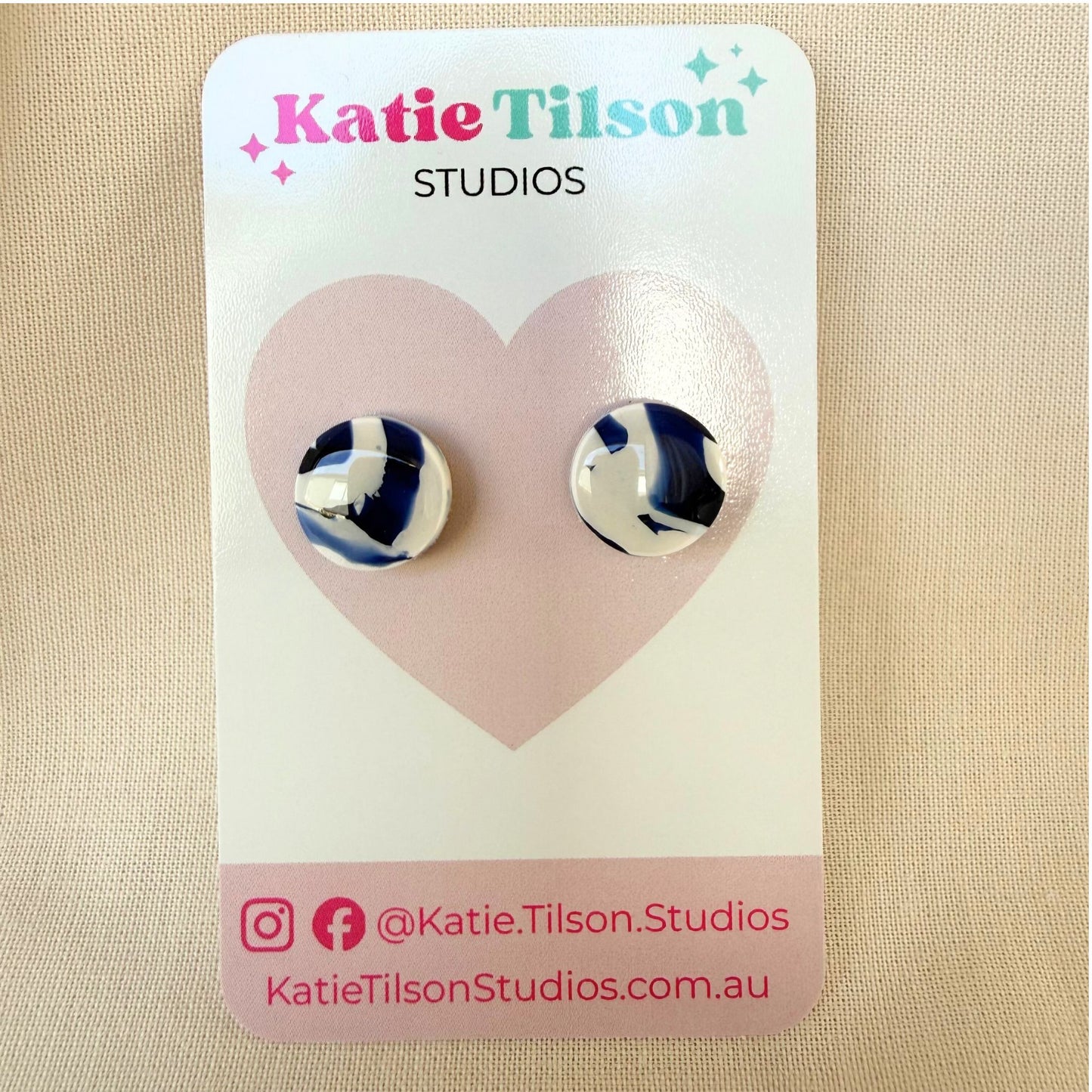 Katie Tilson Studios navy and white swirl design circular stud earrings on an earring card against a beige background.