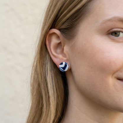 Close-up of a person wearing blue and white patterned stud earrings against a beige background.
