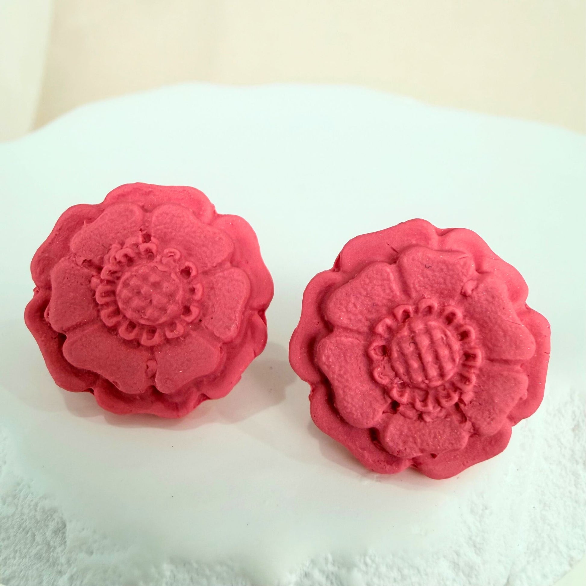 Peach Blossom Australian handmade stud earrings in blush colour floral shape resting on a white stone surface against a beige background.