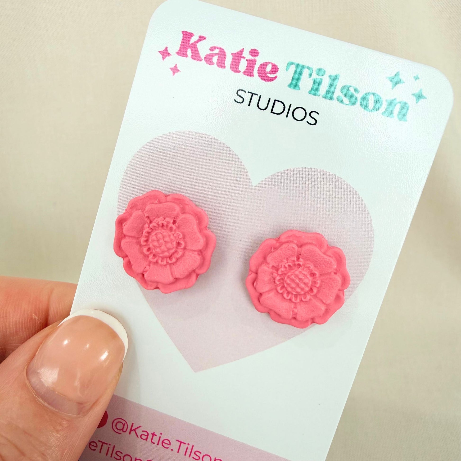Blush coloured flower shaped stud earrings on a Katie Tilson Studios branded earring card held by a hand.