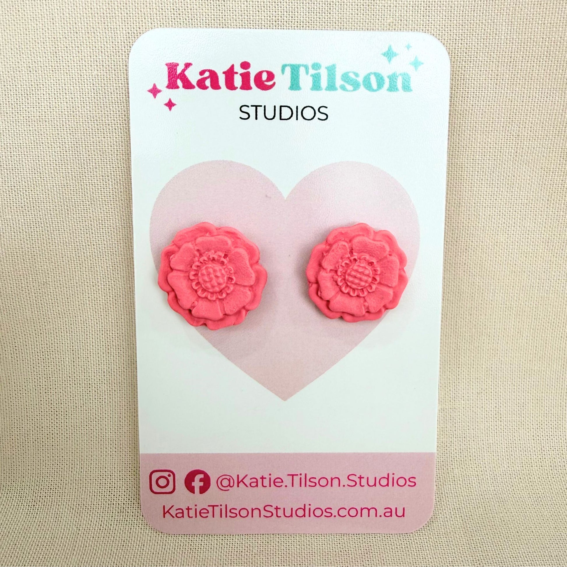 Blush coloured flower shaped stud earrings on a Katie Tilson Studios branded earring card resting against a beige background.
