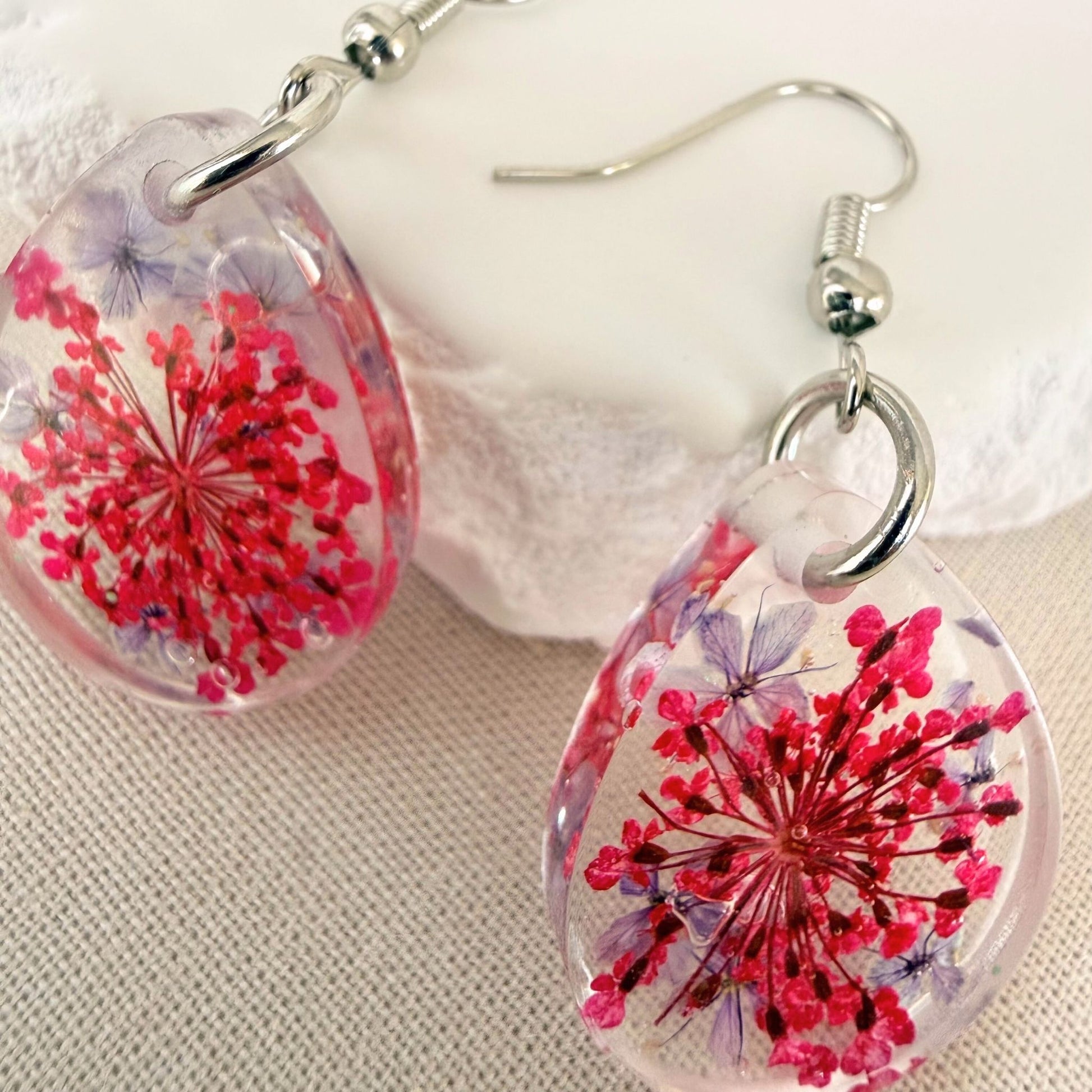 Close up of lightweight handmade dangle earrings Petal Drift Teardrops - pink and purple flowers embedded in clear resin.
