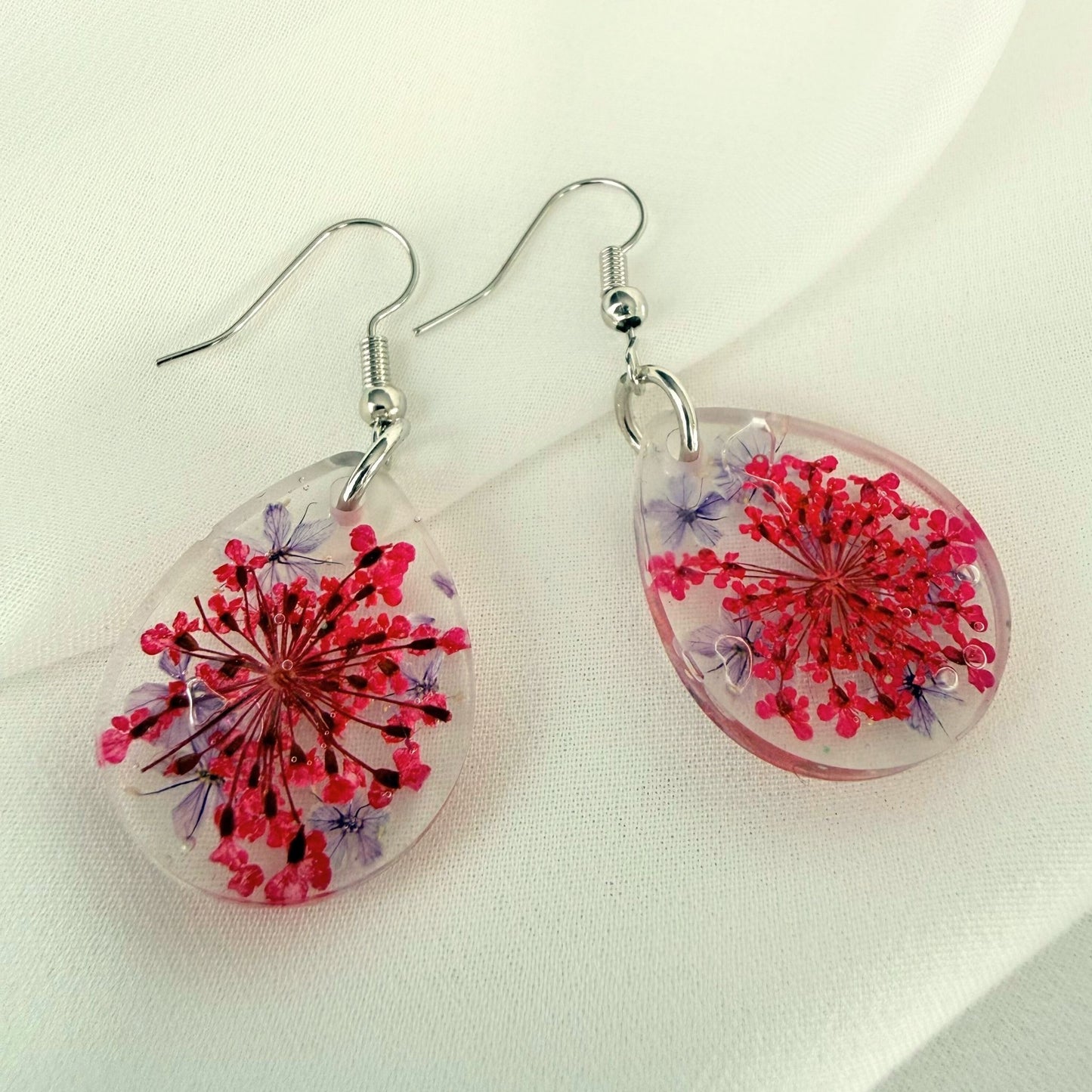 Pair of Petal Drift handmade teardrop earrings in clear resin with embedded flowers design on a light background.
