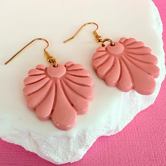Pink fan-shaped dangle earrings with gold hooks on a white stone with a pink background.