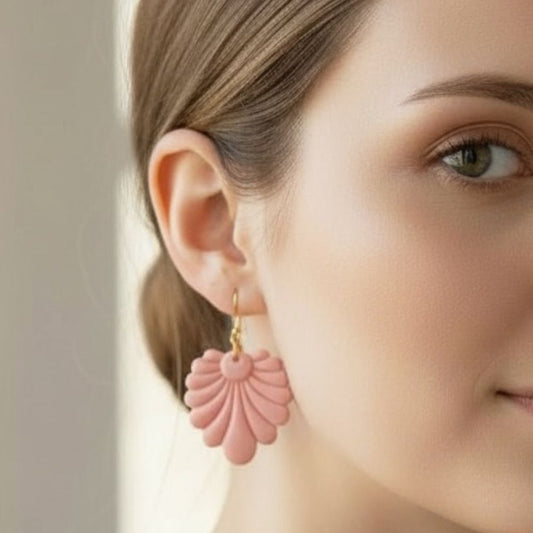 Close-up of a woman wearing pink fan shaped dangle earrings with a neutral background.
