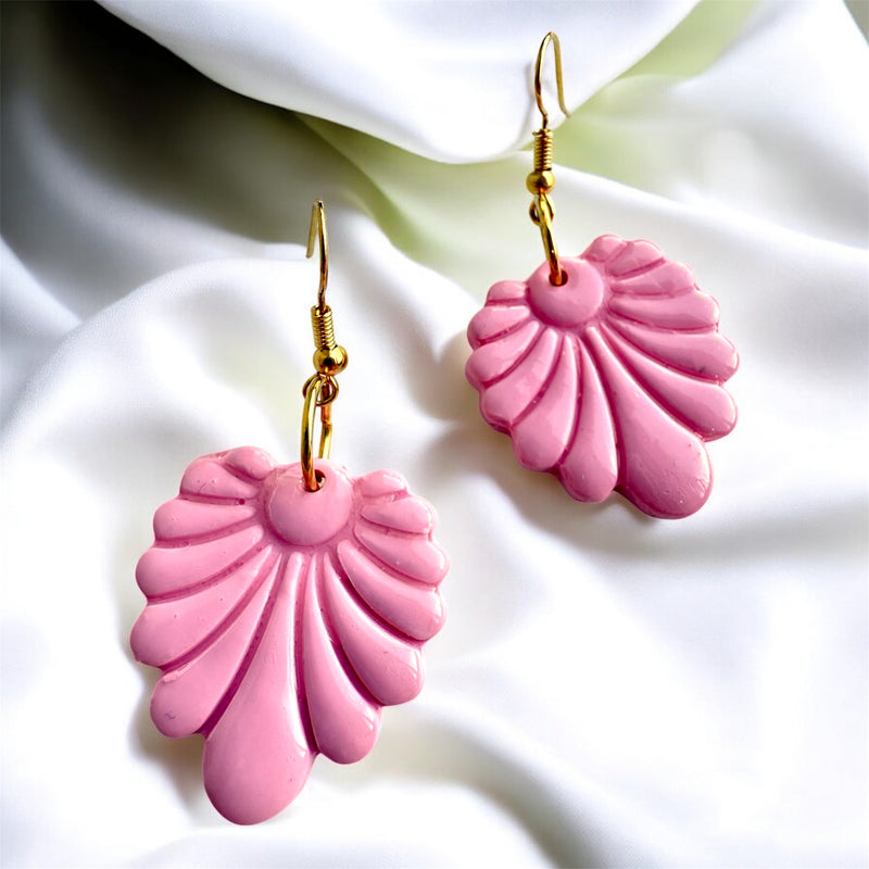 Pink shell-shaped earrings with gold hooks on a white fabric background