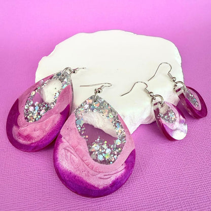 Pink Glow Australian handmade resin dangle earrings with pink and purple design and silver glittery centers on a pink background.