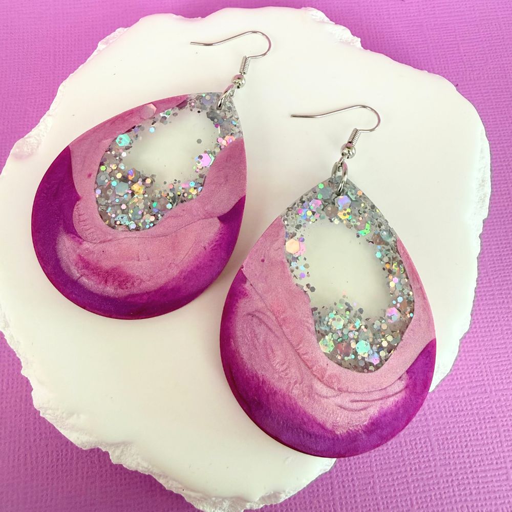 Pink Glow Australian handmade resin dangle earrings in shown in large size resting against a white rock.
