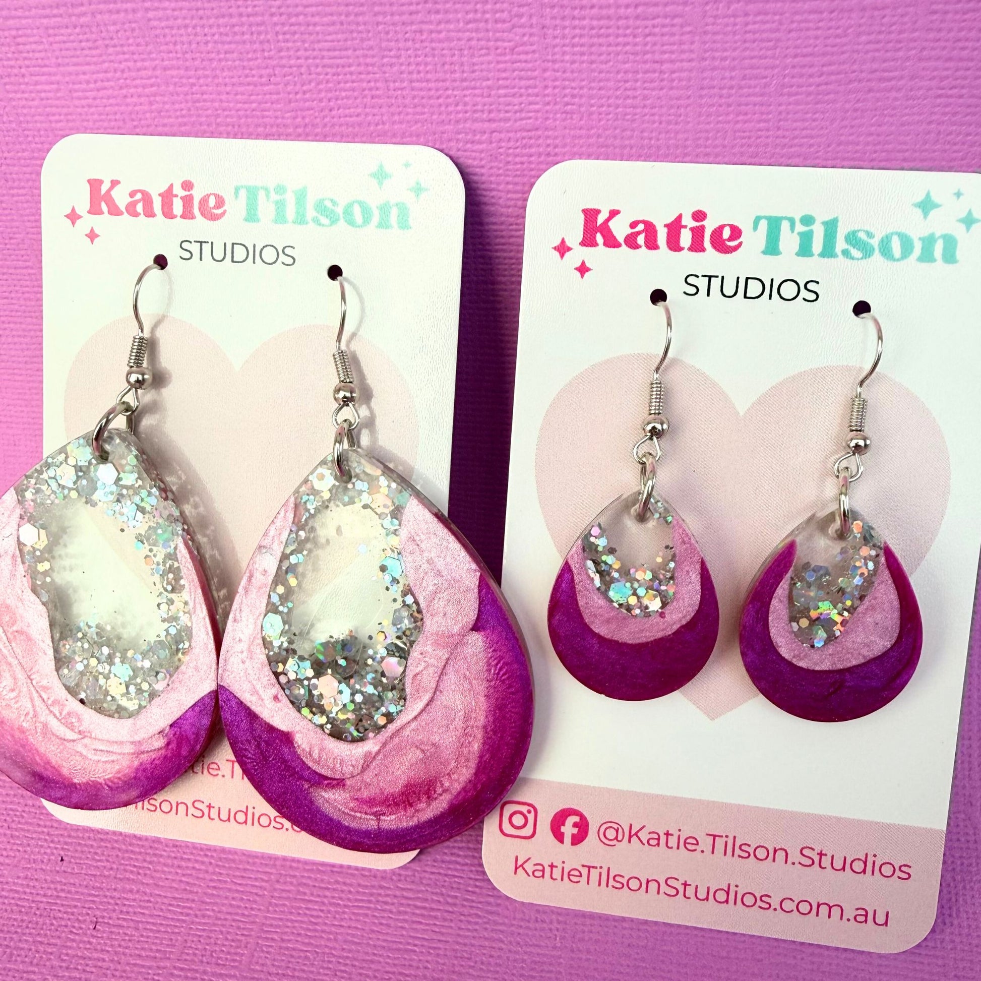 Two pairs of resin earrings on Katie Tilson Studios display cards against a pink background.