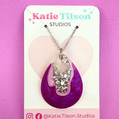 Australian handmade resin necklace with a purple pendant on a Katie Tilson Studios card against a pink background.