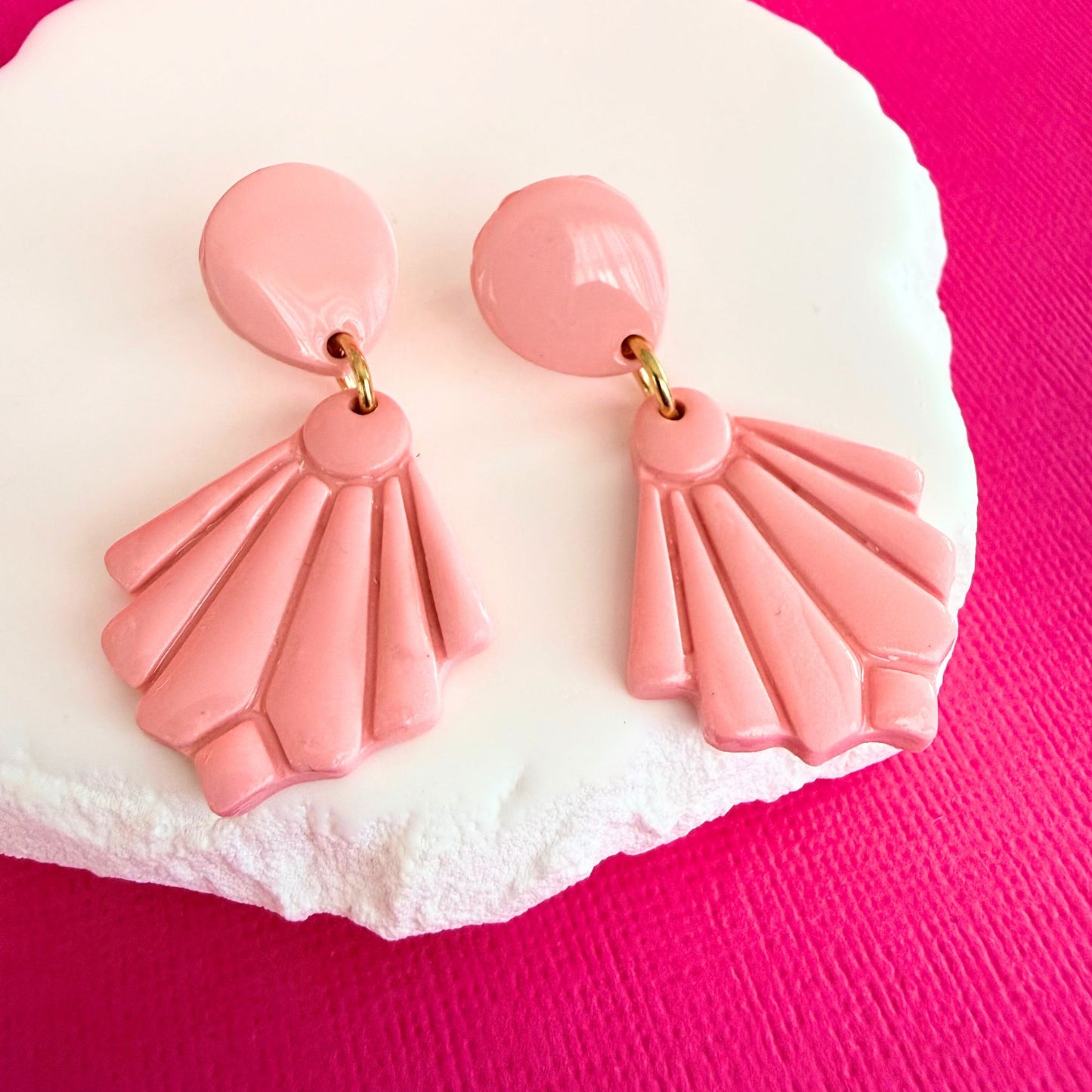 Australian handmade pink fan shaped drop earrings with gold hardware resting on a white stone with a pink background.