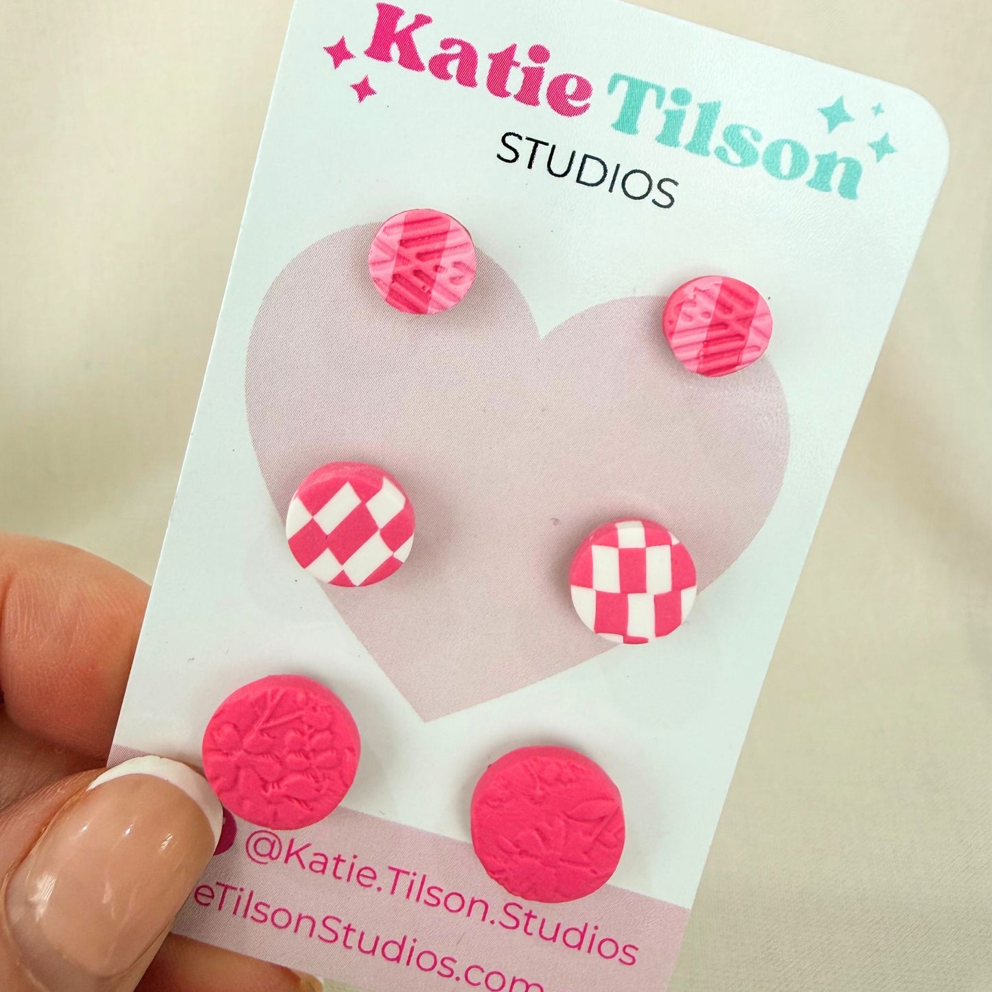 Australian handmade stud earrings trio Pretty In Pink displayed on a Katie Tilson Studios earring card held by a hand.