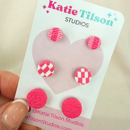 Australian handmade stud earrings trio Pretty In Pink displayed on a Katie Tilson Studios earring card held by a hand.