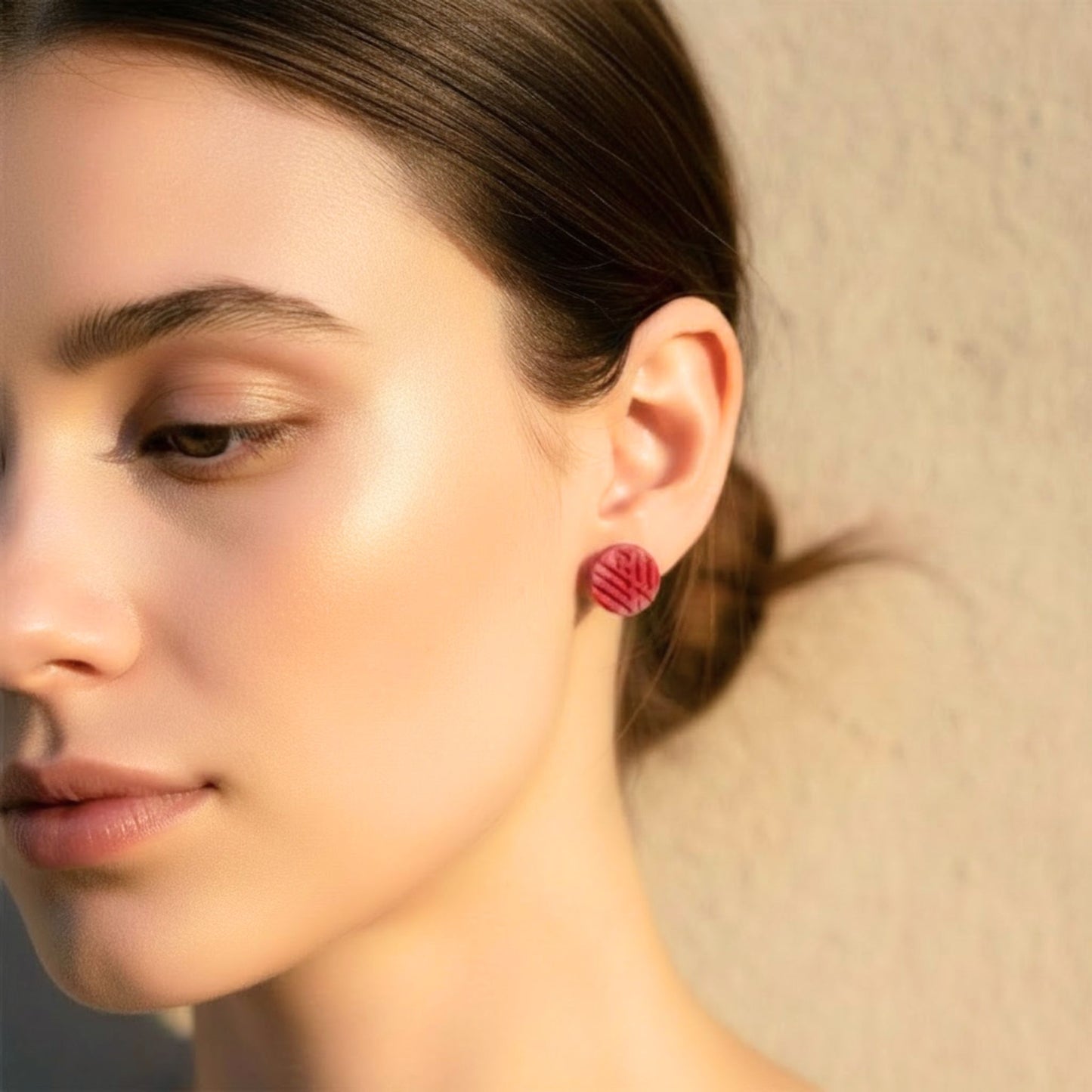 Close-up of a woman wearing small pink toned textured stud earrings from the Pretty In Pink Stud Trio against a neutral background.