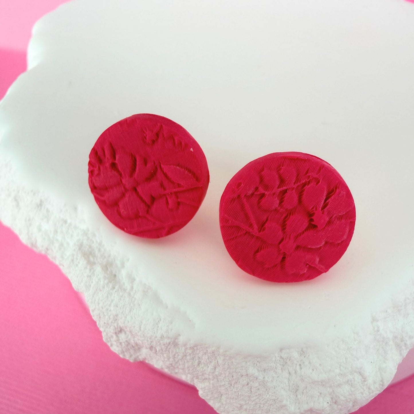 Pink circular stud earrings with floral design on a white stone with pink background.