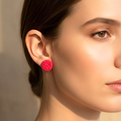 Close-up of a woman wearing pink round stud earrings from the Pretty In Pink Stud Trio with embossed floral design against a neutral background