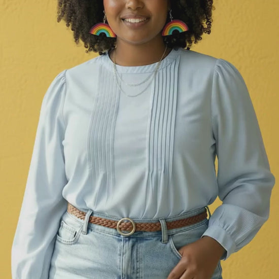 Video of woman wearing rainbow statement earrings and denim outfit turning to show movement of earrings.