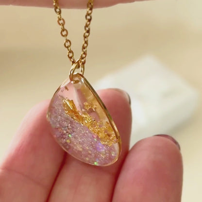 Video of Golden Light Australian handmade resin necklace in clear resin with gold leaf and sparkle details on a gold chain.