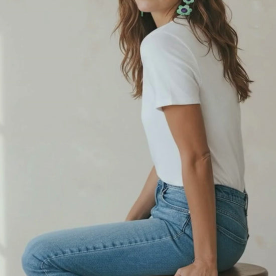 Video of a woman wearing mint and purple flower statement earrings and a casual blue jeans and white t-shirt outfit.
