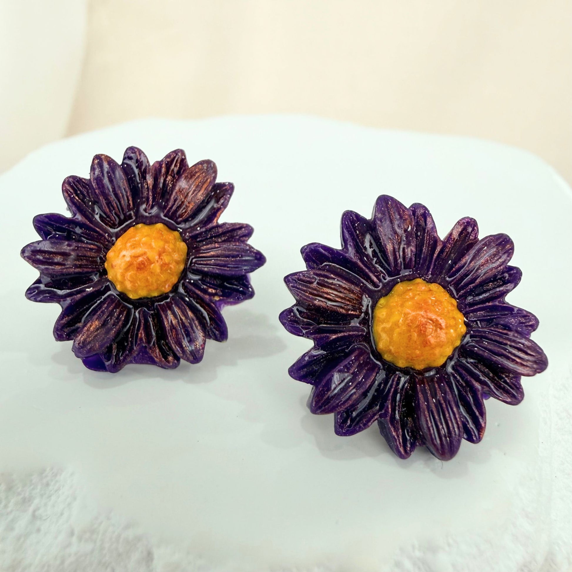 Purple flower-shaped stud earrings with yellow centers on a white surface.