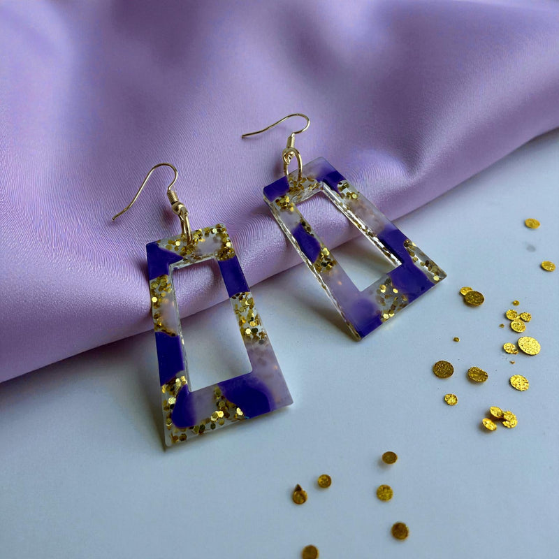 Pair of earrings with purple and gold design on a purple fabric background