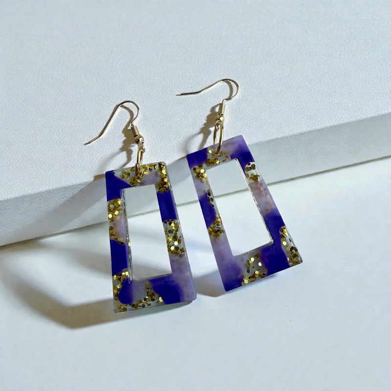 Pair of purple and gold earrings with geometric design on a light background.