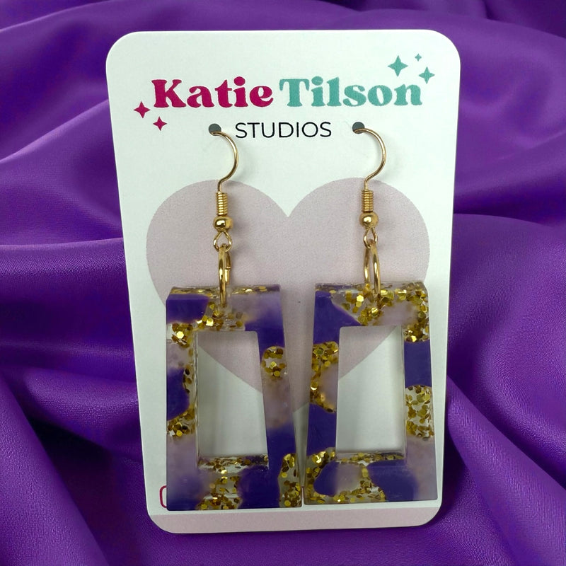 Katie Tilson Studios Purple Haze resin earrings on a purple fabric background