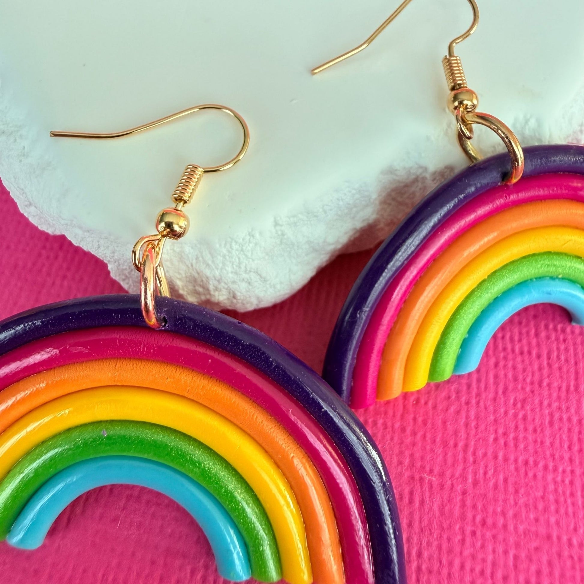 Close up of colorful rainbow-shaped Australian handmade dangle earrings on a pink background,