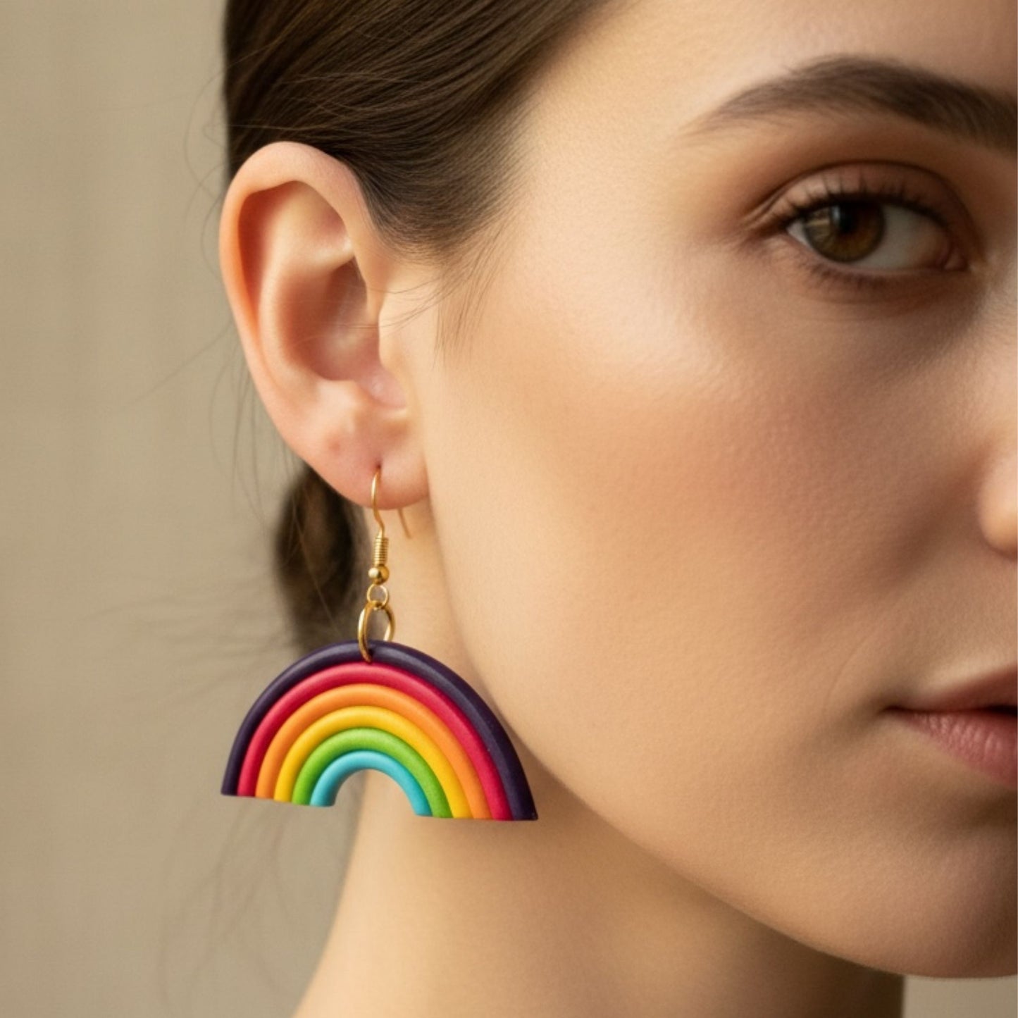 Close-up of a woman wearing Australian handmade colorful rainbow earrings with gold hooks against a neutral background.