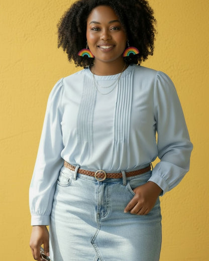 Woman wearing a light blue blouse and jeans with rainbow dangle earrings against a yellow background.