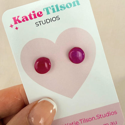 Raspberry colour circular stud earrings on a Katie Tilson Studios card held by a hand.