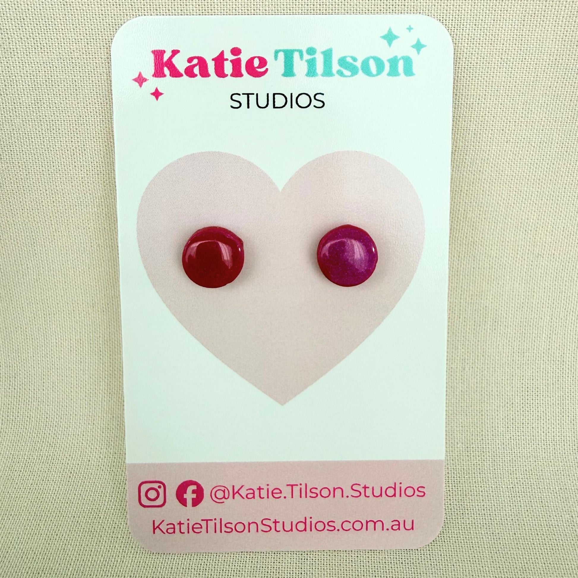 Raspberry colour circular stud earrings on a Katie Tilson Studios card against a beige background.