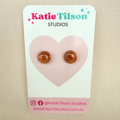 Rose gold glitter circular stud earrings on a Katie Tilson Studios card against a beige background.