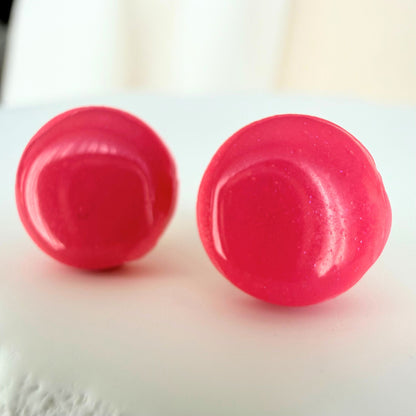 Glossy rose pink stud earrings in a circular shape design resting on a white surface.