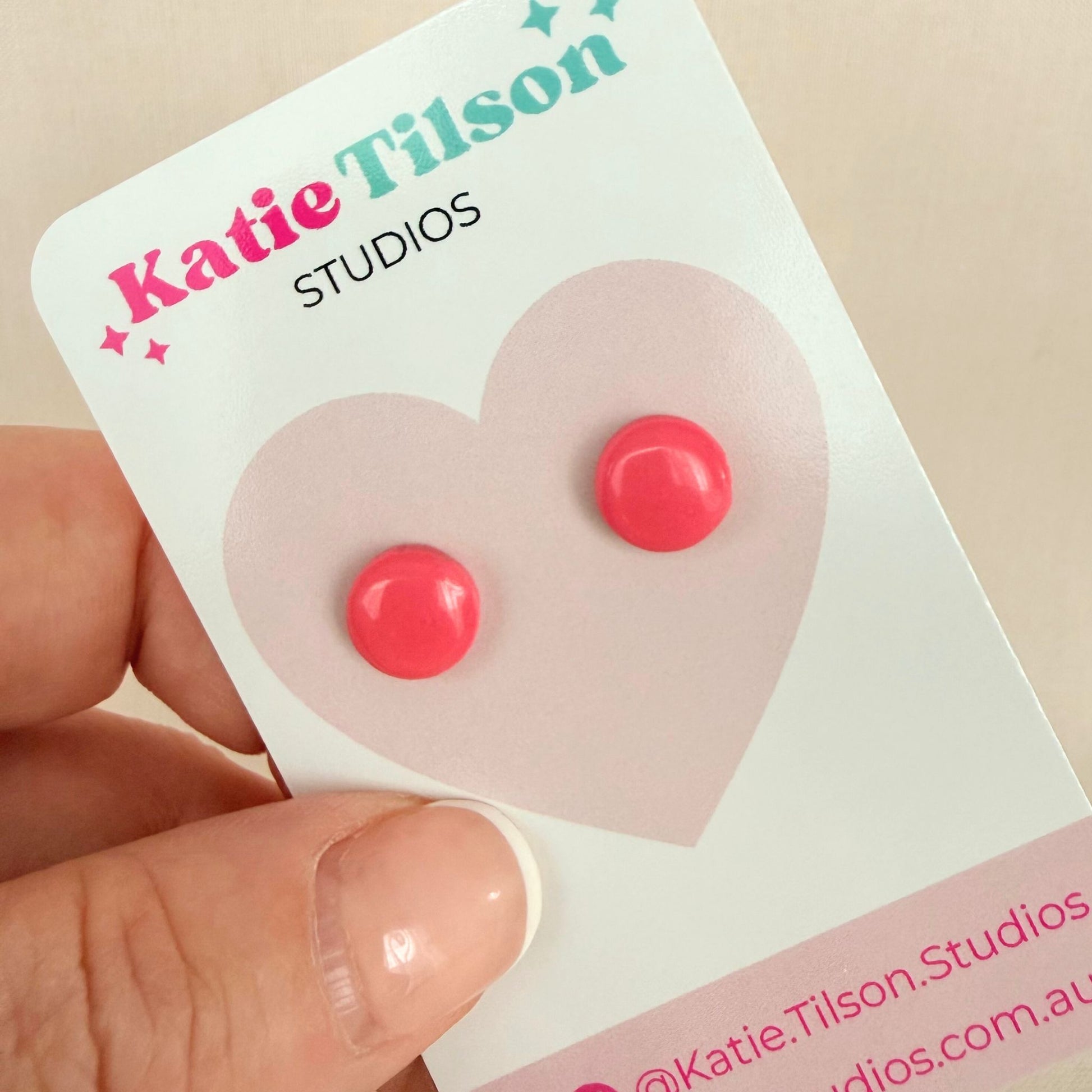 Pink circular stud earrings on a Katie Tilson Studios card held by a hand.