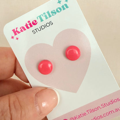 Pink circular stud earrings on a Katie Tilson Studios card held by a hand.